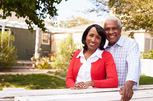 Senior black couple look to camera outside their new house